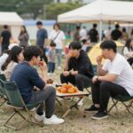 2026년 광주 금남로 차 없는 거리 걷자잉 축제 광주 금남로 걷자잉 축제에서 사람들이 길거리 캠핑 의자에 앉아 군고구마를 나눠 먹으며 즐거워하는 모습