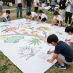 야외 공원에서 열린 어린이 가족 예술축제에서 아이들이 거대한 그림을 함께 그리고 있는 모습