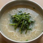 시원한 냉메밀국수 한 그릇, 고추냉이와 간 무가 올려져 있고 국물이 맑게 보인다.