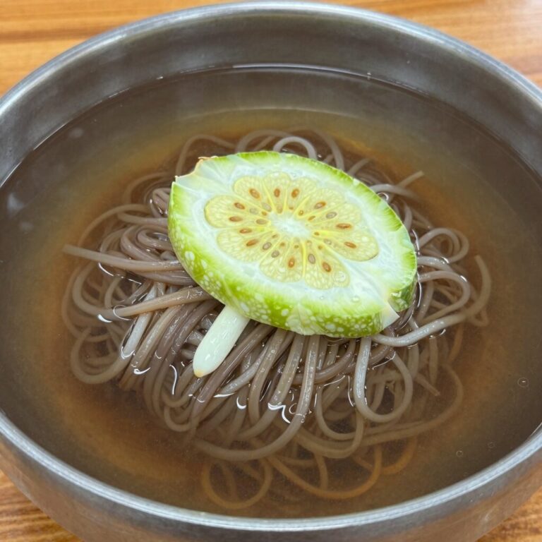 일산 고자리냉면 물냉면에 오이가 산더미처럼 올려져 있는 모습, 시원한 육수와 배도 보인다